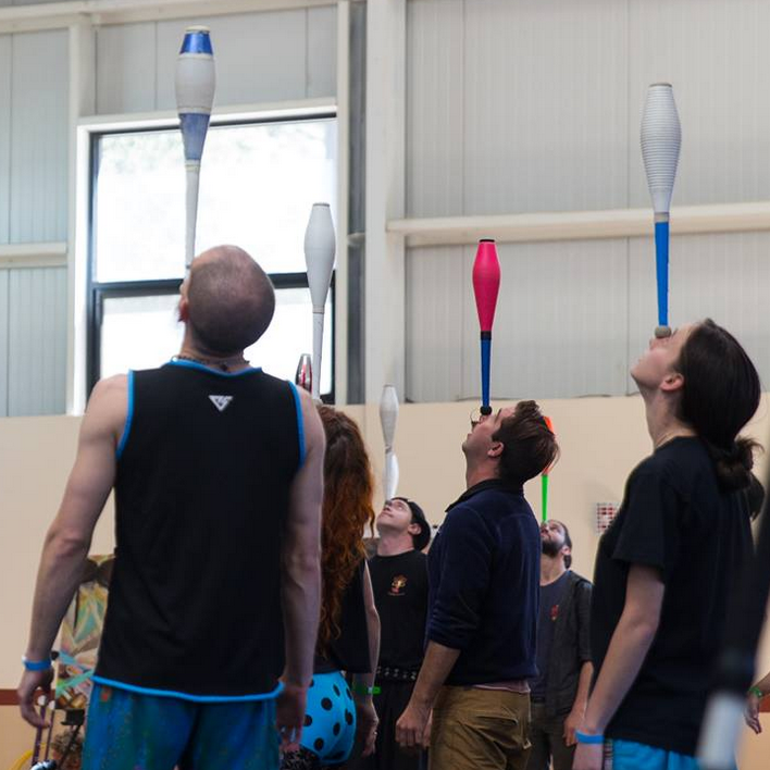 several jugglers all stand in concentration, each carefully balancing a juggling club upright on their face
